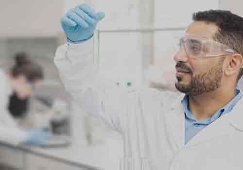 Experienced young male chemist in lab coat holding rack and analyzing sample in test tube while working in modern laboratory