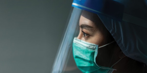 Female front-line care worker in mask and face shield combatting COVID-19 pandemic