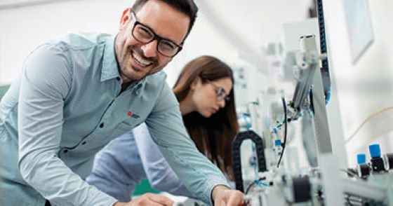 Smiling man in blue shirt with woman lab tech in the background